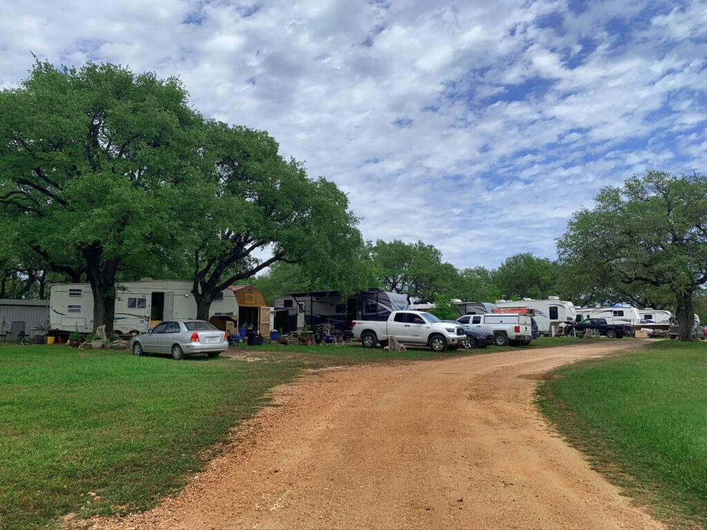 A wide-angle shot of multiple RVs parked in a neatly organized row at Rising Spirit RV Park in Liberty Hill, Texas.