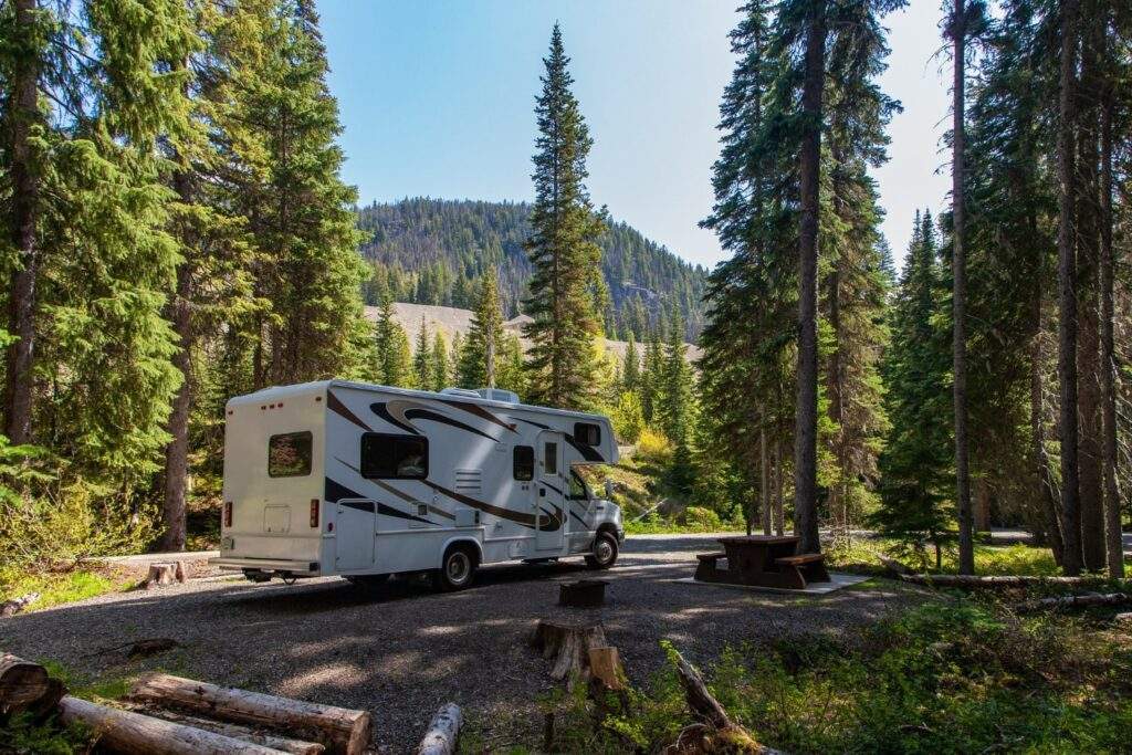 beautiful motor home parked in the middle of a forest near wooden bench